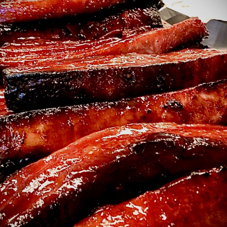 Close-up of glistening, dark red Chinese BBQ pork ribs, stacked and ready to serve.
