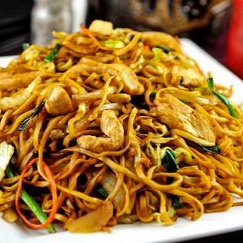 A large plate of Chinese chow mein noodles with chicken, cabbage, and carrots.