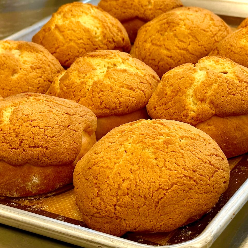 A tray of freshly baked, golden-brown pineapple buns with a crumbly topping.