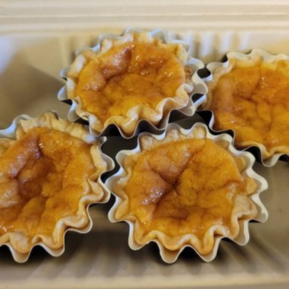 Four golden-brown Chinese egg tarts in white fluted paper cups, in a light brown container.