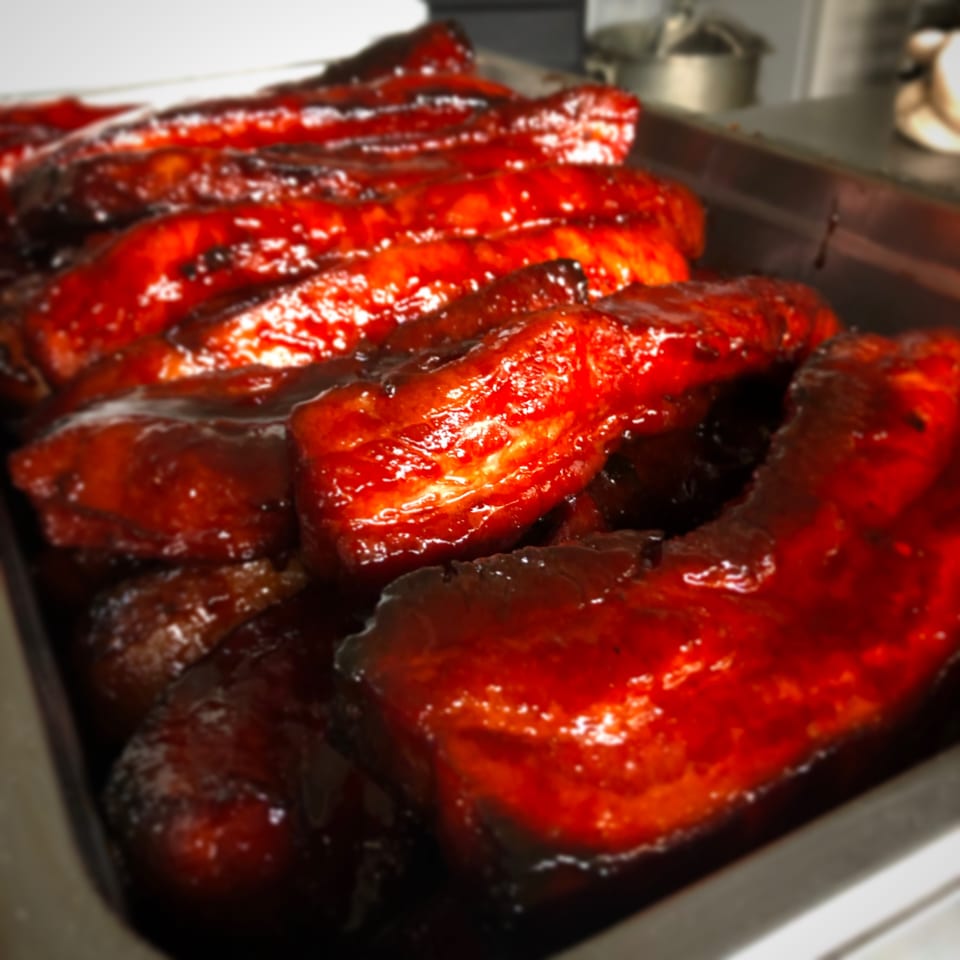 Close-up of glistening, red char siu pork ribs in a metal tray at Only Ono BBQ.