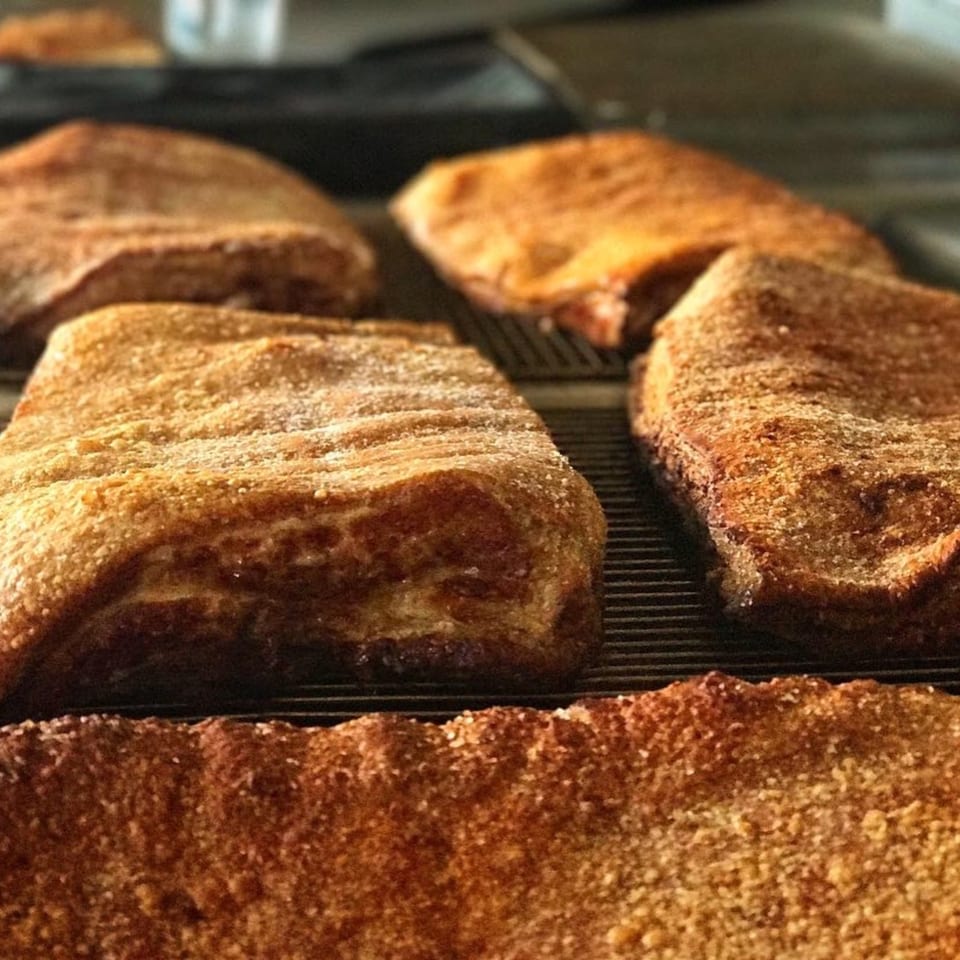 Several golden-brown, sugar-dusted Chinese pastries, possibly Only Ono BBQ's signature dessert, cooling on a wire rack.