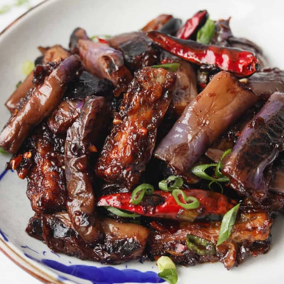 Close-up of Chinese eggplant with red chilies and green onions in a glossy dark sauce.