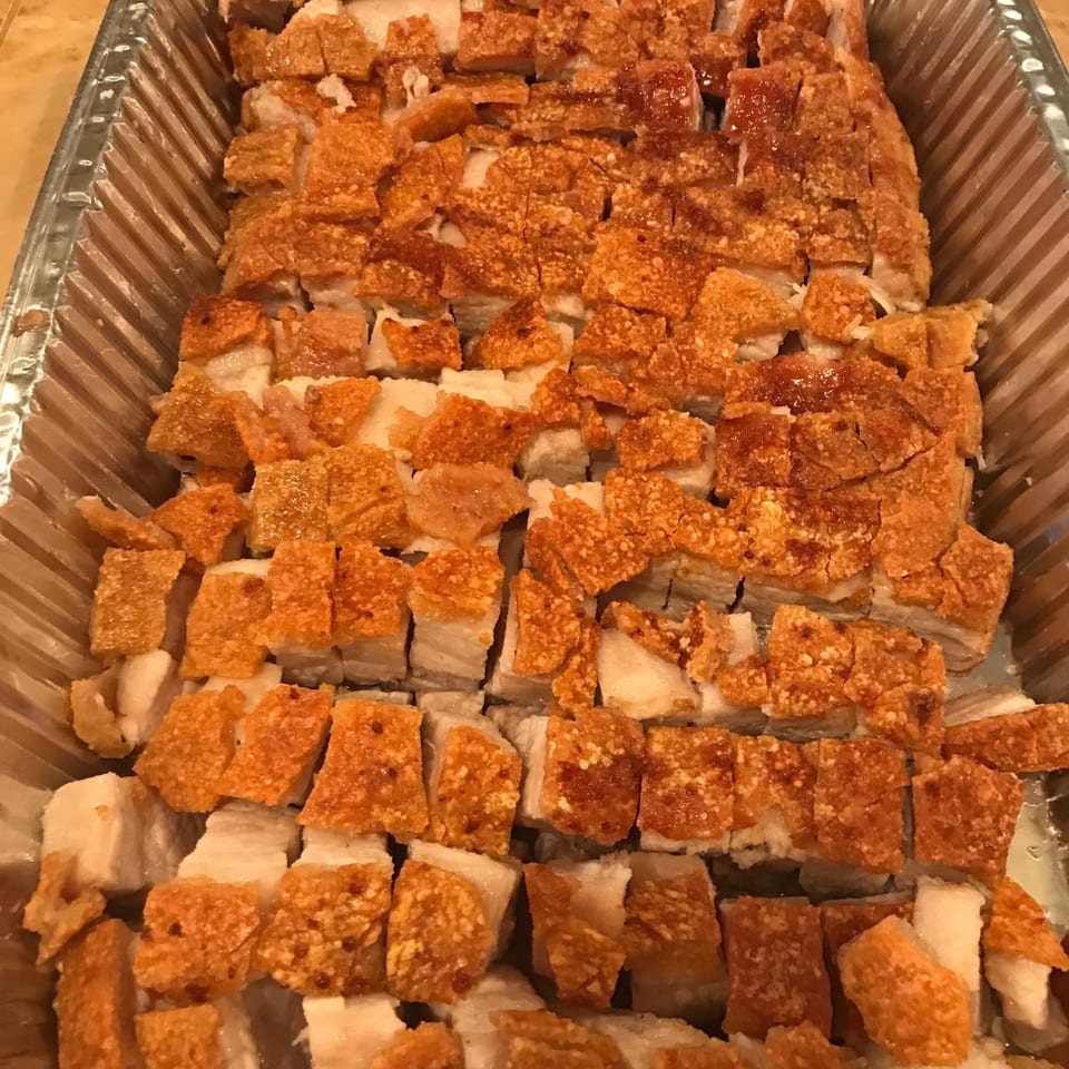 Close-up of crispy roasted pork belly, cut into squares, in a foil pan.