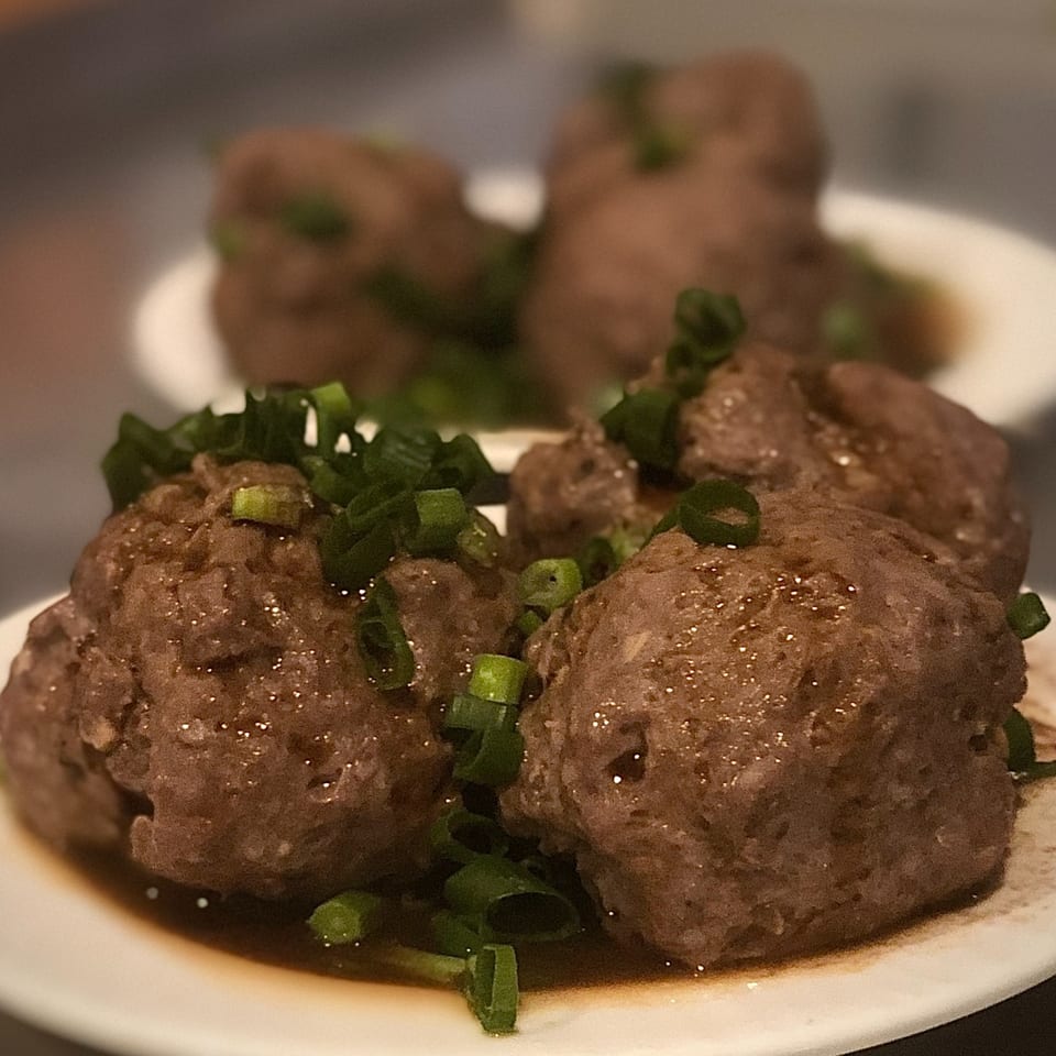 Close-up of several Chinese meatballs, glistening with sauce and topped with chopped green onions.